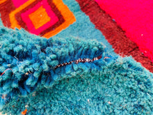 Load image into Gallery viewer, Close-up of a tufted blue rug with visible wear and contrasting white and black weft threads.
