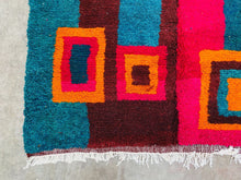 Load image into Gallery viewer, Detail shot of a colorful Moroccan rug featuring bold geometric shapes in red, orange, and teal.
