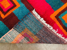 Load image into Gallery viewer, A textured corner of a multicolored Moroccan rug, highlighting the intricate weaving and fringe detail.
