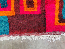 Load image into Gallery viewer, Corner of a Moroccan rug folded over to reveal the underside weaving patterns, with multicolored threads and textures.
