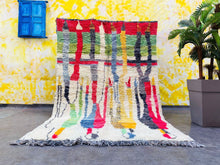 Load image into Gallery viewer, Full view of the colorful Moroccan Berber rug laid out on a gray floor against a bright yellow wall with a blue window, embodying a cheerful and artistic vibe.
