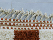 Load image into Gallery viewer, Corner view of a Moroccan checkered rug with orange and white patterns, highlighting its unique texture and design.
