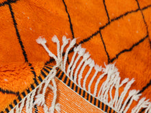 Load image into Gallery viewer, Orange handmade Moroccan carpet with soft wool texture and black line patterns, a standout piece for bold interior designs.


