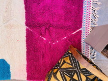 Load image into Gallery viewer, Corner detail of a Moroccan rug with a focus on the fringe and patterned border against a textured floor.
