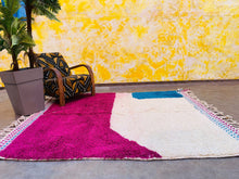 Load image into Gallery viewer, Full view of a Moroccan rug in a room setting, showing its design and placement in a living space with a plant and chair.
