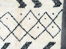 Load image into Gallery viewer, Macro shot of a Beni Ourain Moroccan rug&#39;s black diamond pattern on white wool, showcasing the unique tribal symbols and plush texture.
