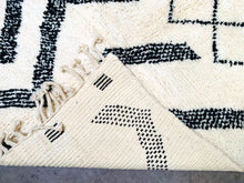 Load image into Gallery viewer, Corner detail of a Beni Ourain rug with black and white patterns, revealing the hand-knotted fringe and the rug’s authentic, thick weave.
