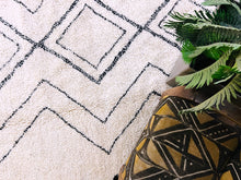 Load image into Gallery viewer, Close-up view of a handmade Moroccan rug with black diamond patterns on a white wool background, detailed with fringe edges.
