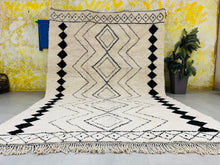 Load image into Gallery viewer, Handmade Moroccan Berber rug with black patterns and fringes, displayed vertically against a vibrant yellow wall.
