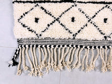 Load image into Gallery viewer, Full view of a black and white Moroccan rug on a grey surface, with rich textures and a bold design.
