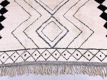 Load image into Gallery viewer, The edge of a Moroccan rug with a black diamond design, showcasing the hand-knotted fringe detailing.
