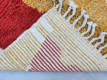 Load image into Gallery viewer, Close-up texture detail of a Moroccan wool rug showing rich red and mustard yellow weave with intricate white and blue line patterns.
