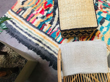 Load image into Gallery viewer, Overhead view of a Moroccan wool rug alongside a wicker chair and a woven basket, illustrating a cozy home setting.
