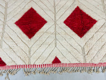 Load image into Gallery viewer, Elegant Moroccan Berber Beni Ourain rug laid out to display its symmetrical red diamond design with white high-pile wool and intricate red and white fringe detailing along the edges.
