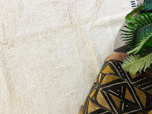 Load image into Gallery viewer, Detail of the edge of a Moroccan wool rug, featuring hand-knotted fringe and a bold black and white geometric border.
